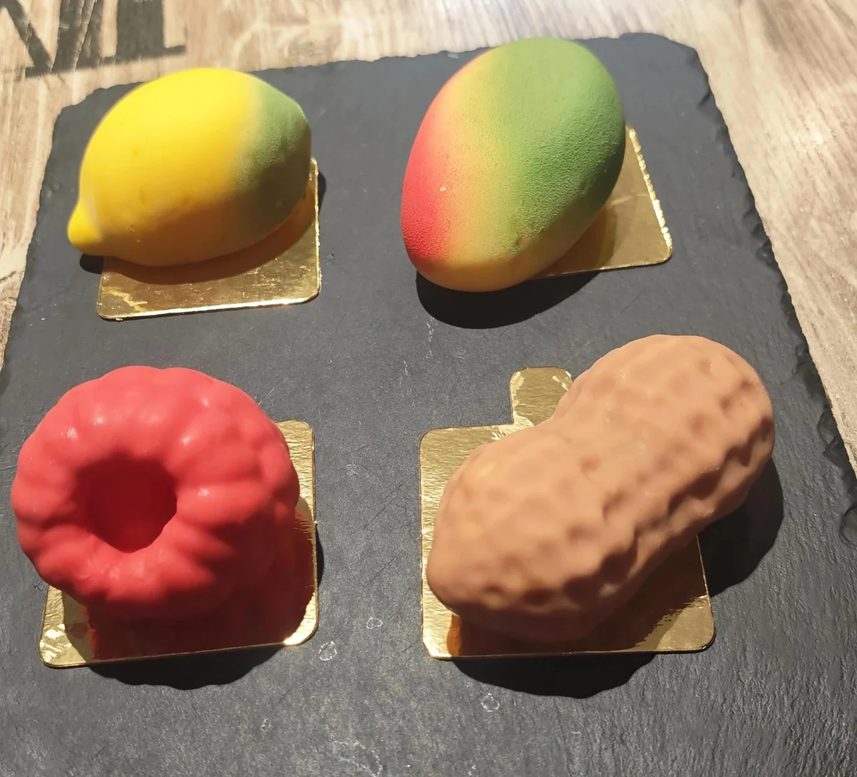 Quatre pâtisseries trompe-l’œil en forme de citron, mangue, framboise et cacahuète